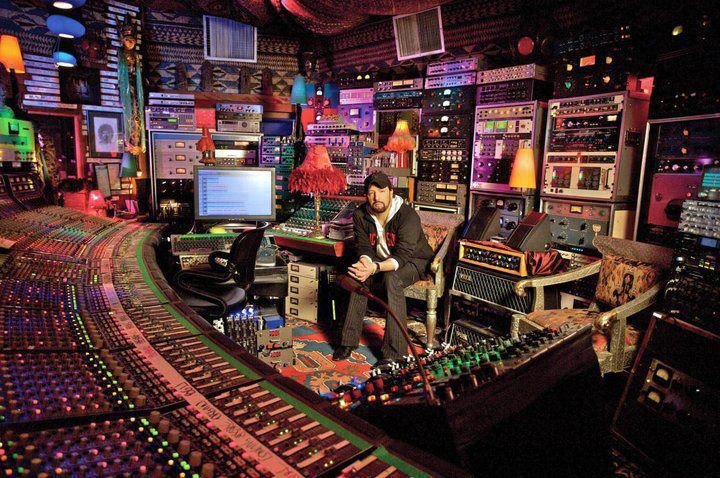 a man in a recording studio surrounded by musical instruments and mixing equipment, with his hands on the ground