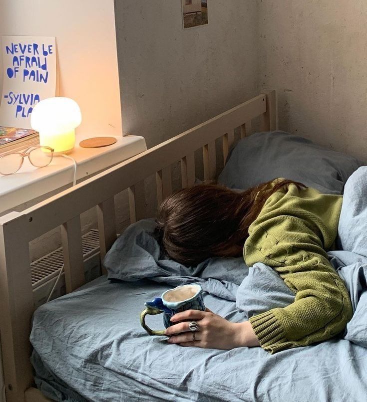 a woman laying on top of a bed next to a night stand with a lamp