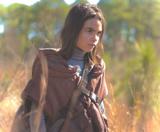 a young woman standing in tall grass with her back to the camera and looking off into the distance