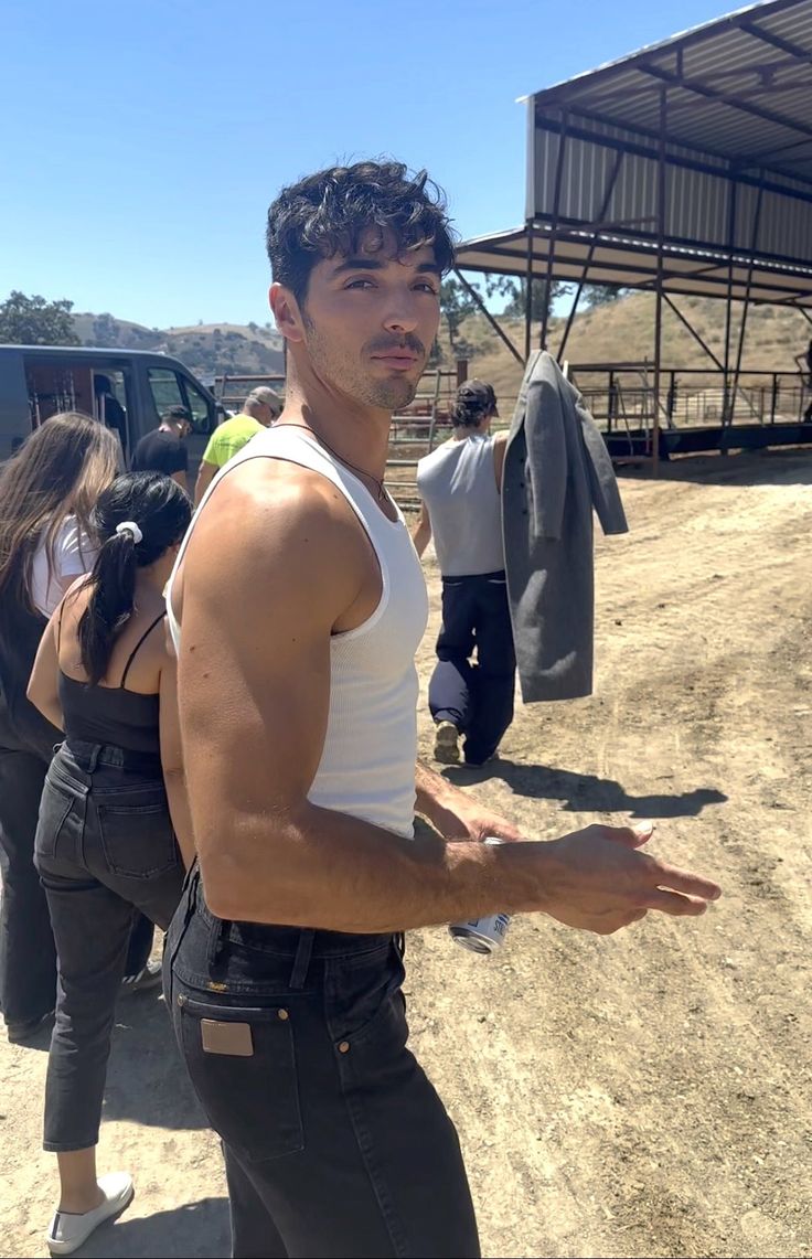 a man in white tank top standing on dirt road next to other men and women