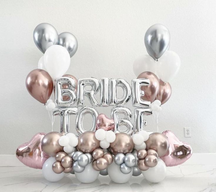 the bride to be balloon arch is decorated with silver, pink and white balloons that spell out their names