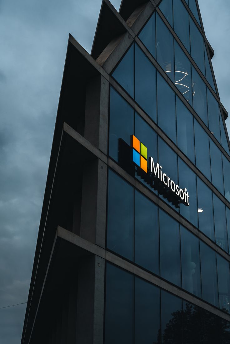 a tall building with windows and a microsoft logo on it's side, against a cloudy sky