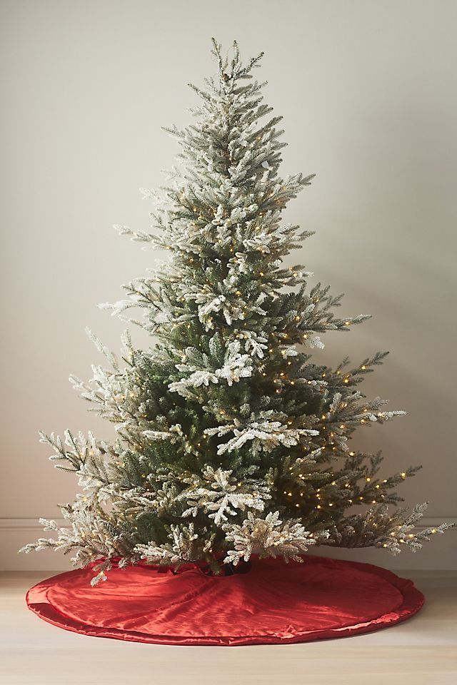 a white christmas tree with snow on the top and red blanket around it, in front of a wall