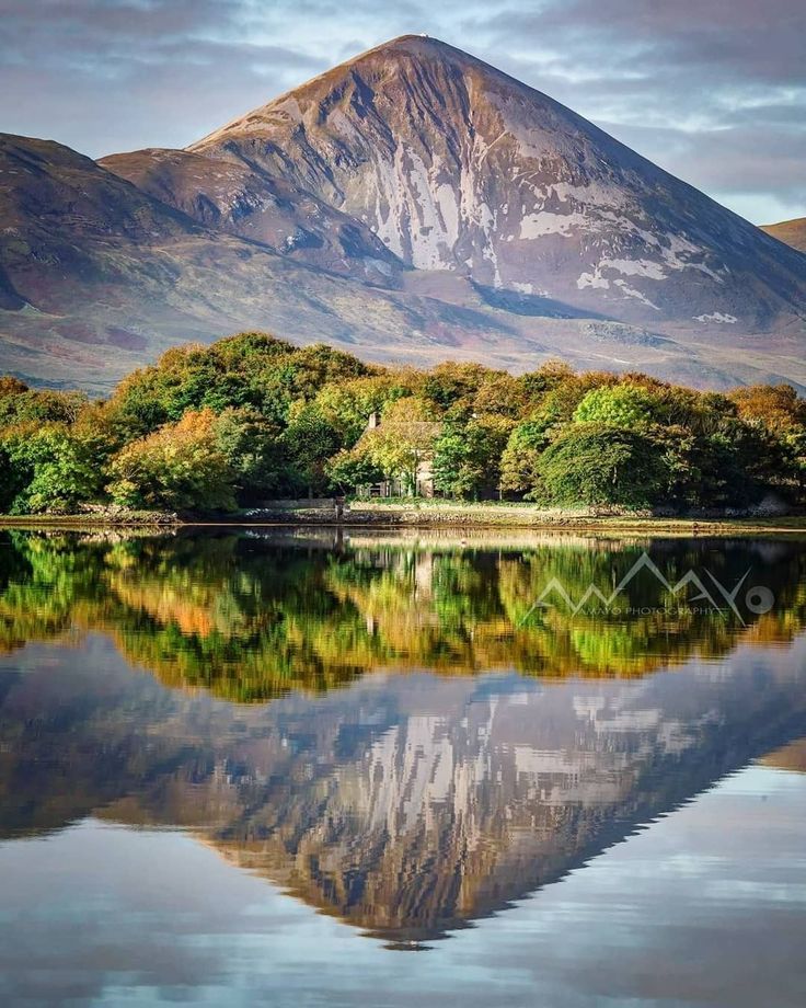 the mountain is reflected in the still water on the lake's surface, with trees and shrubs surrounding it