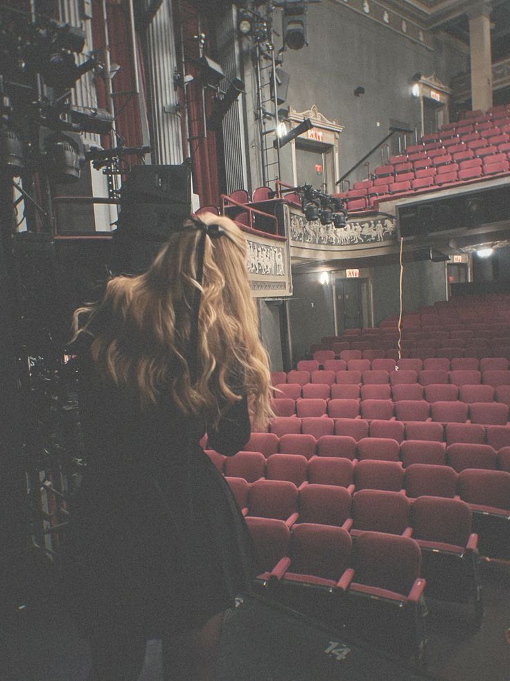 a woman standing in front of an empty auditorium filled with red velvet seats, looking at the stage