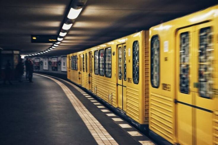 a yellow train traveling down tracks next to a loading platform at a subway station with people standing on the platform