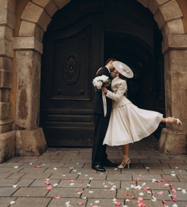 a bride and groom kissing in front of a doorway with rose petals on the ground