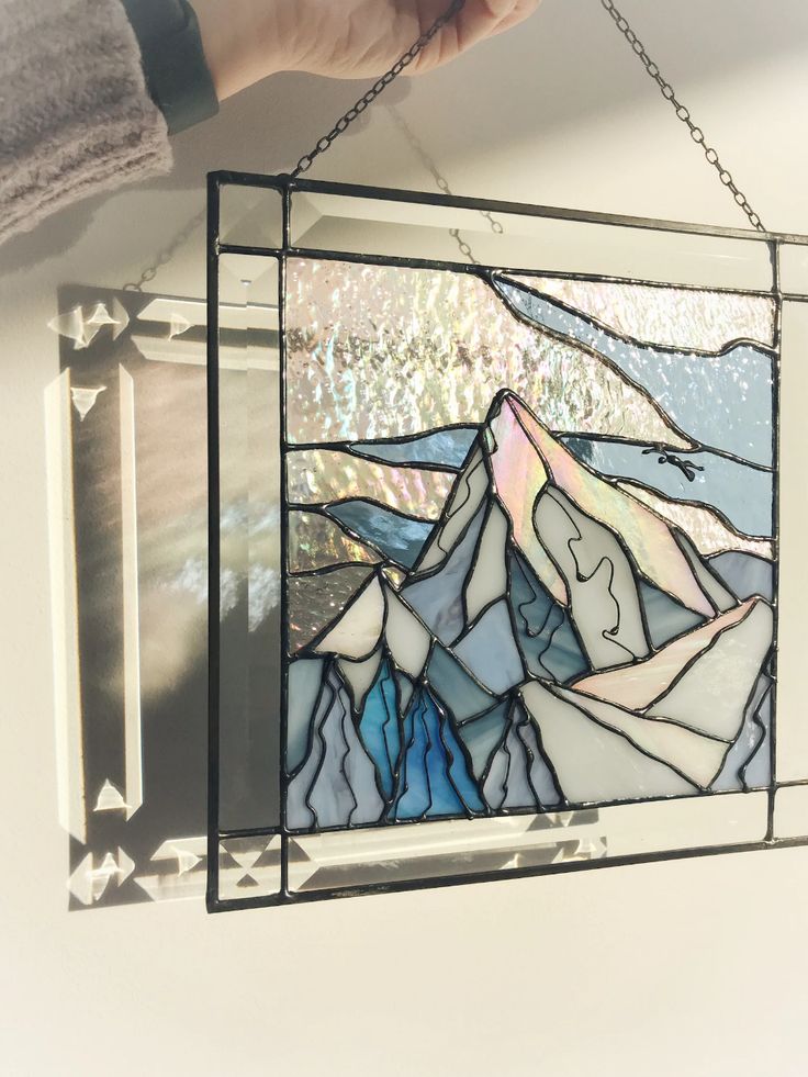 a hand holding a stained glass window hanging from a chain with mountains in the background