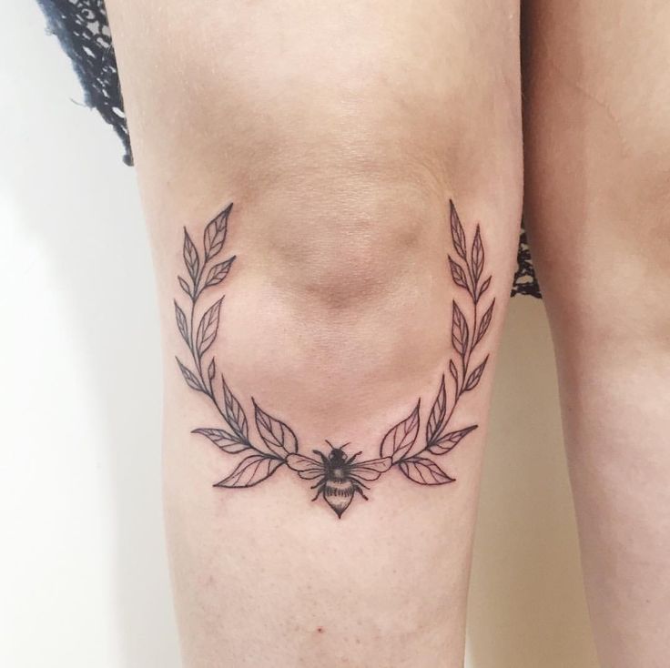 a woman's leg with a tattoo on it that has leaves and a bee