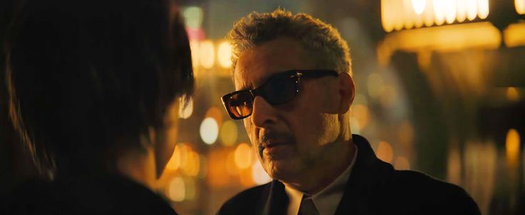 a man wearing sunglasses and a suit talking to another person in the dark at night