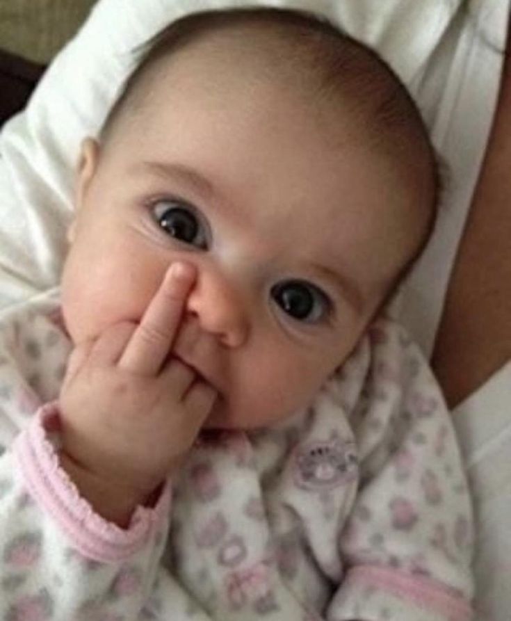 a baby laying on top of a woman's stomach holding her hand up to her mouth