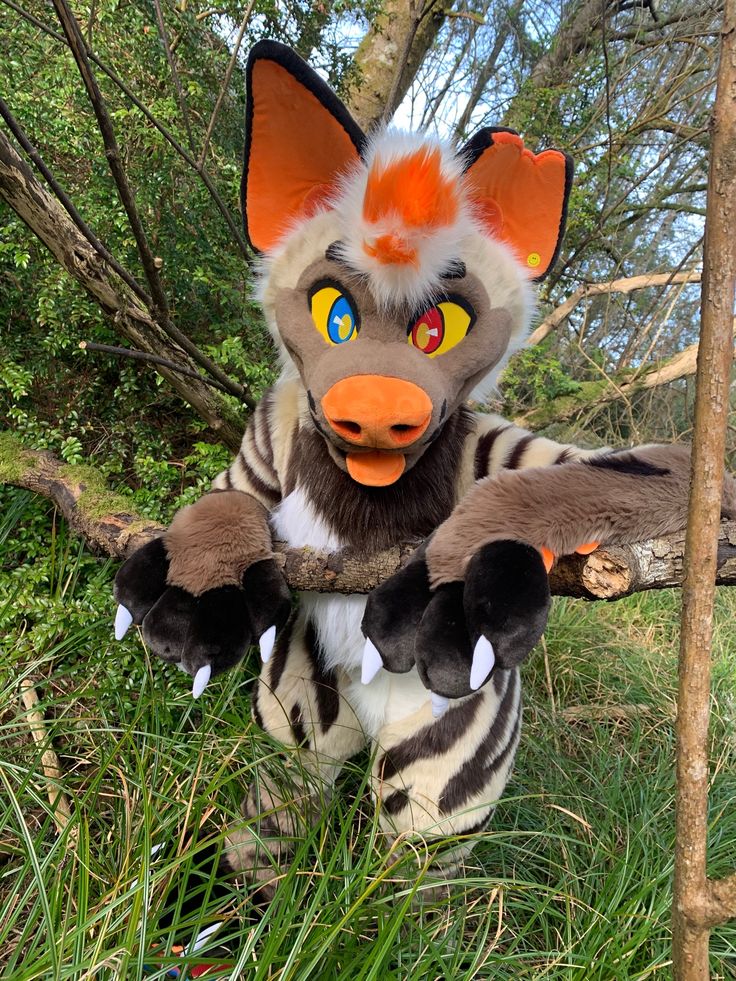 a stuffed animal is sitting in the grass next to a tree and wearing an orange nose