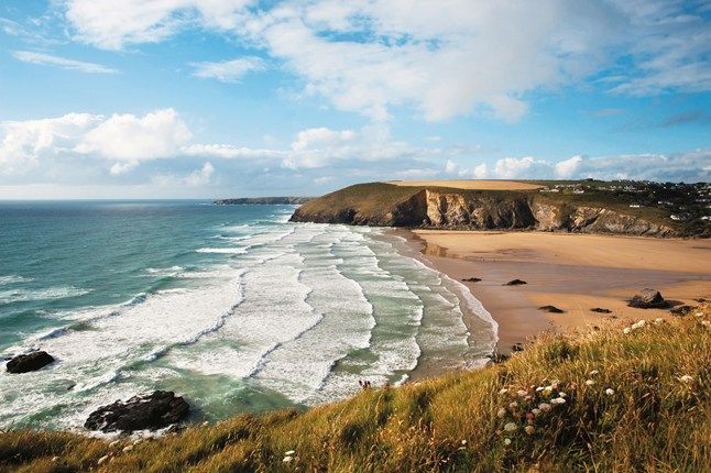 an ocean view with waves crashing on the shore and cliffs in the distance, under a partly cloudy blue sky