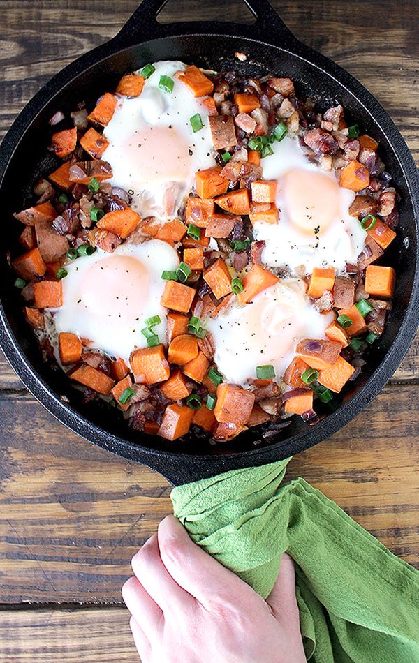 a skillet filled with eggs and vegetables on top of a wooden table next to a person's hand