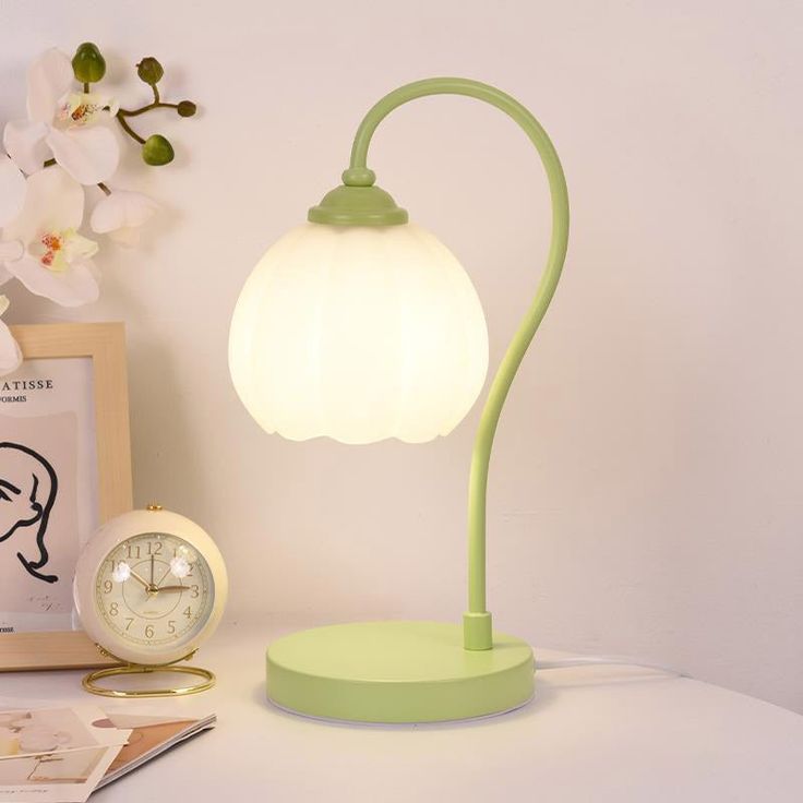 a green lamp sitting on top of a white table next to a clock and flowers