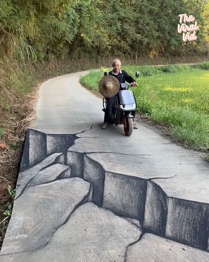 a man riding on the back of a scooter down a road next to a lush green field