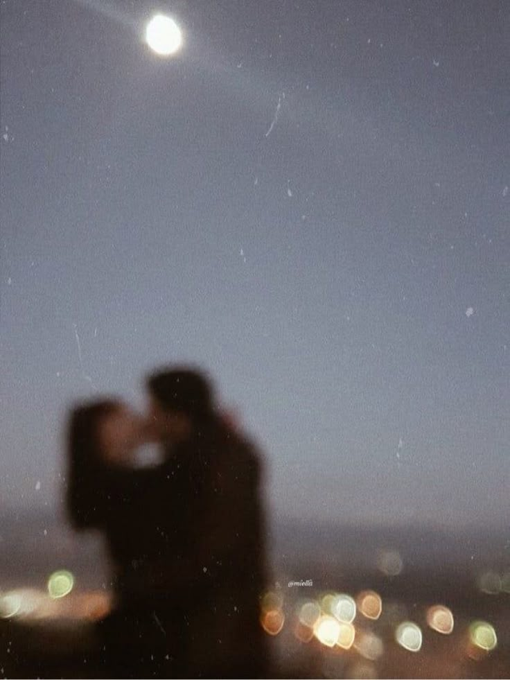 two people standing in front of a window at night, with the moon above them