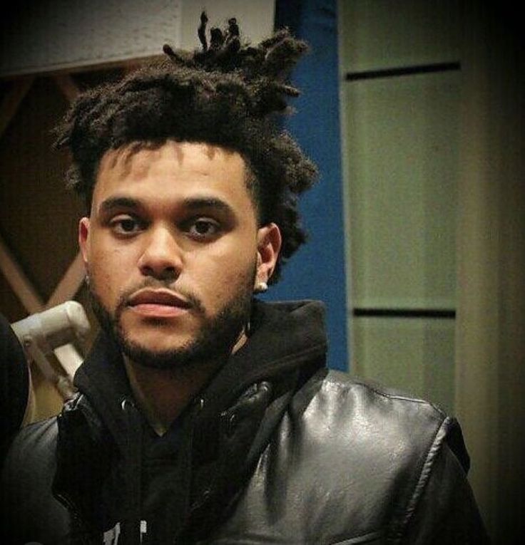 a man with dreadlocks standing in front of a wall and looking at the camera