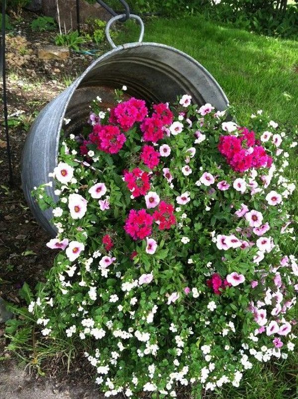 some pink and white flowers are in a pot on the ground near a metal barrel