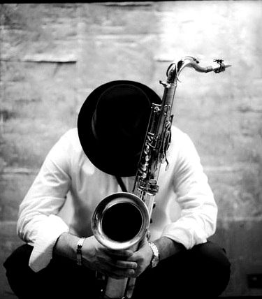 a man sitting on the ground holding a saxophone in his hands and wearing a hat