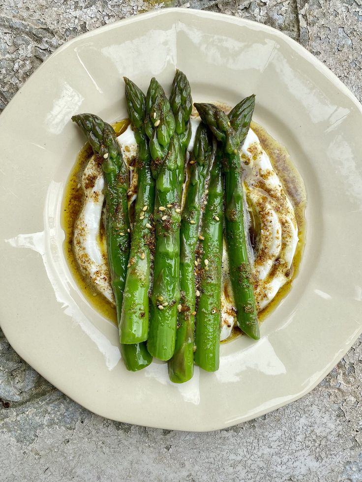 asparagus on a white plate topped with cream and seasoning sitting on a stone surface