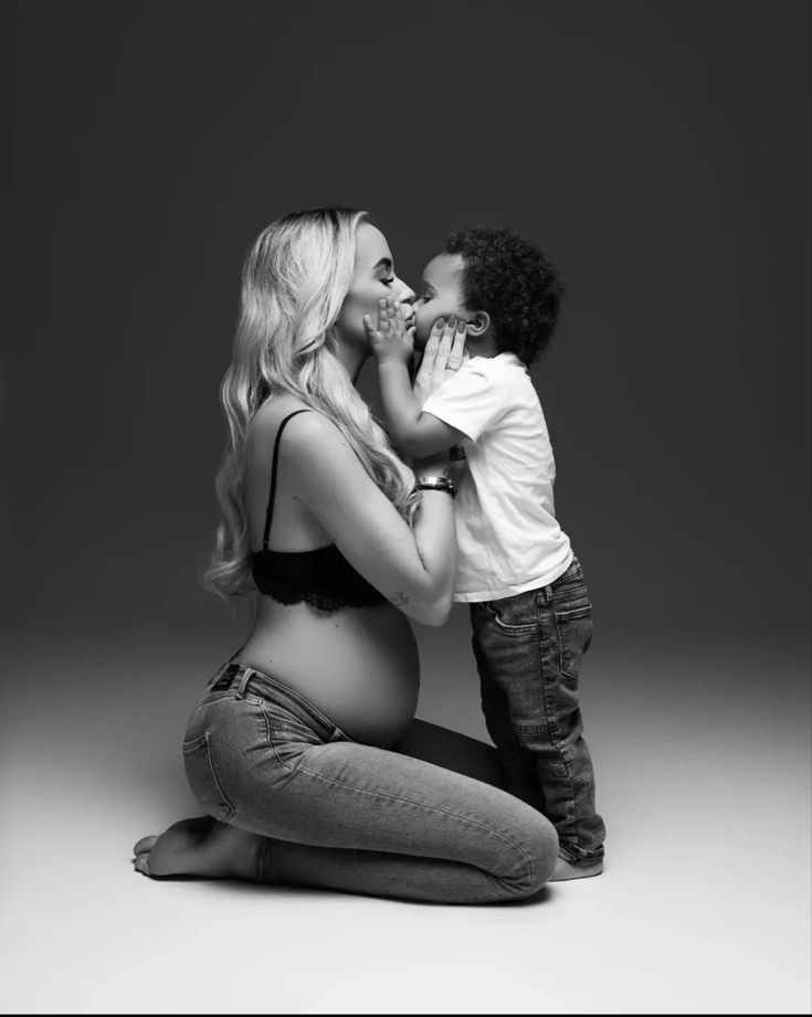 a black and white photo of a mother kissing her son's cheek while sitting on the floor