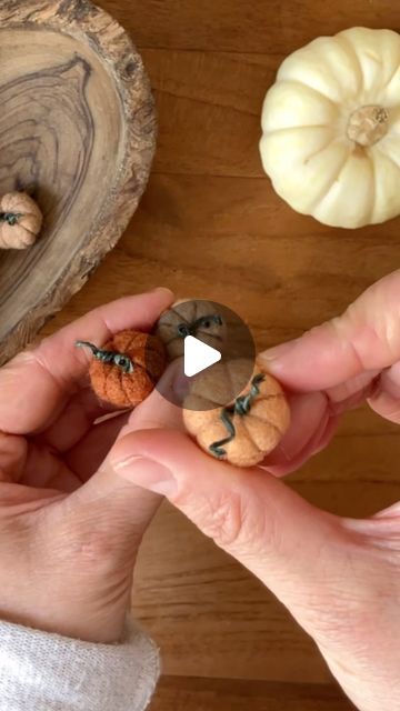 a person holding two small pumpkins in their hands next to some smaller ones on the table