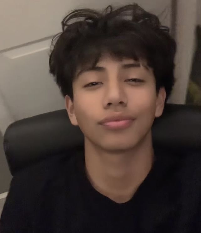 a young man sitting in a chair with his eyes closed and hair blowing in the wind