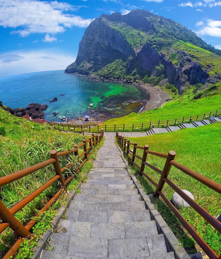 stairs lead down to the beach with green hills in the background and blue water on either side