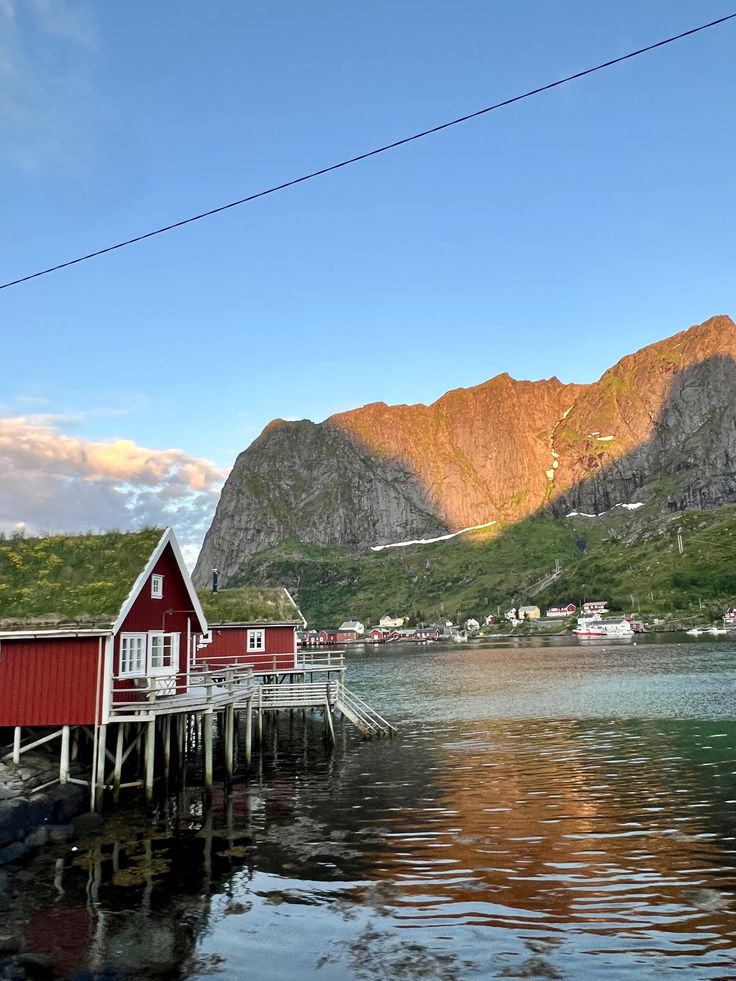 a red house sitting on top of a lake next to a lush green mountain range