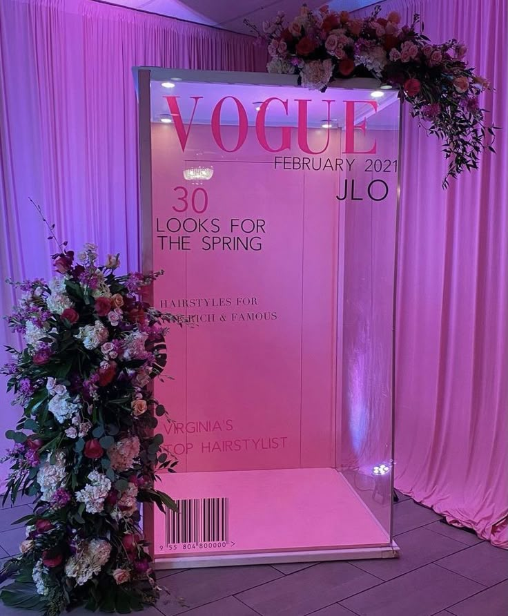 a pink display case with flowers and greenery in front of a curtained backdrop