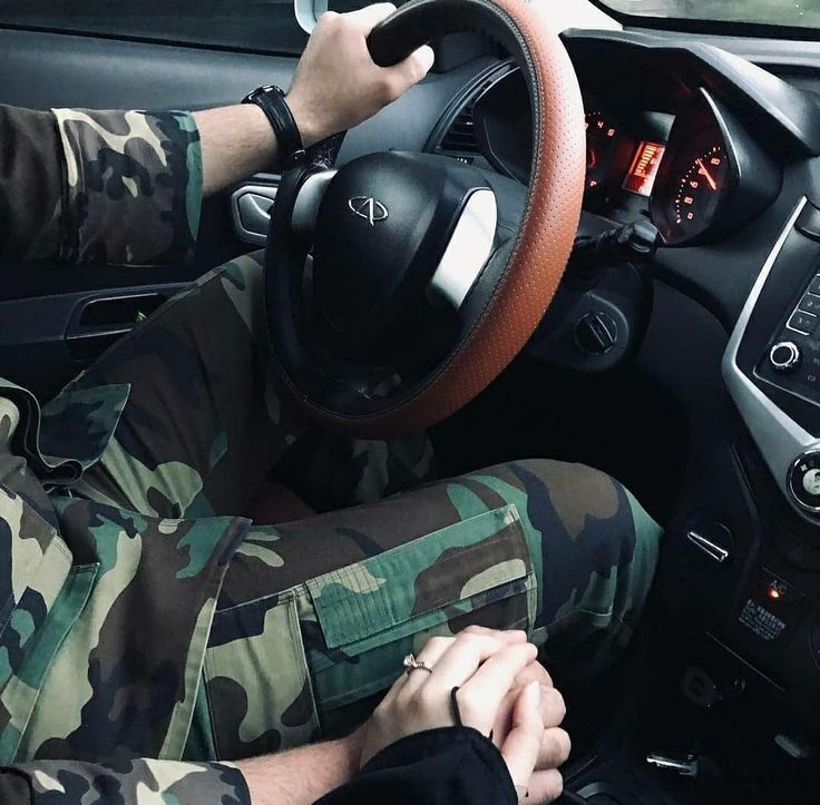 a man in camouflage driving a car with his hands on the steering wheel