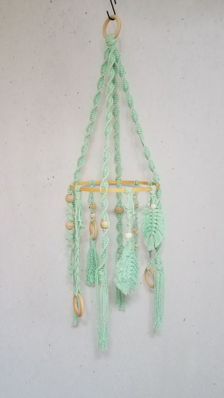 a green crocheted wall hanging with beads and tassels attached to it