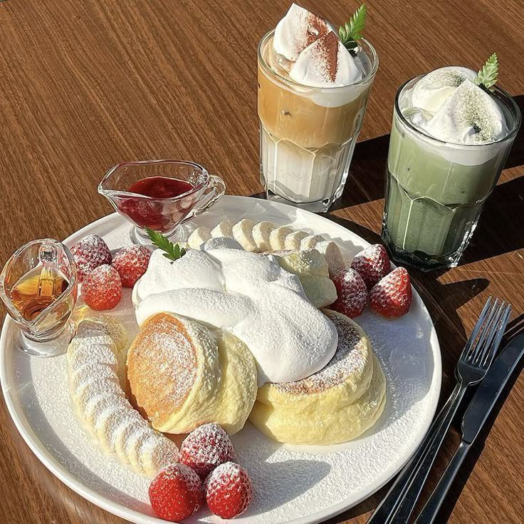 a white plate topped with pastries covered in powdered sugar next to two drinks