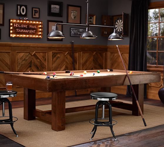 a pool table with three stools in front of it and several lights hanging from the ceiling