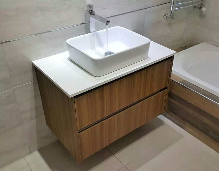 a white sink sitting on top of a wooden cabinet next to a bathtub in a bathroom