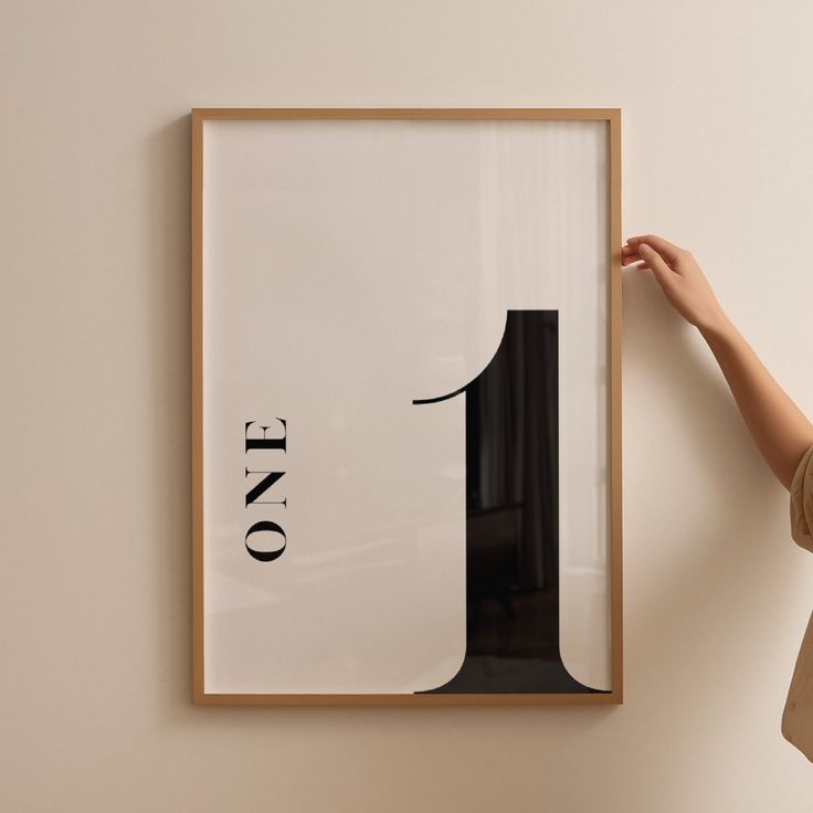 a person holding up a framed poster with the number one on it in front of a wall