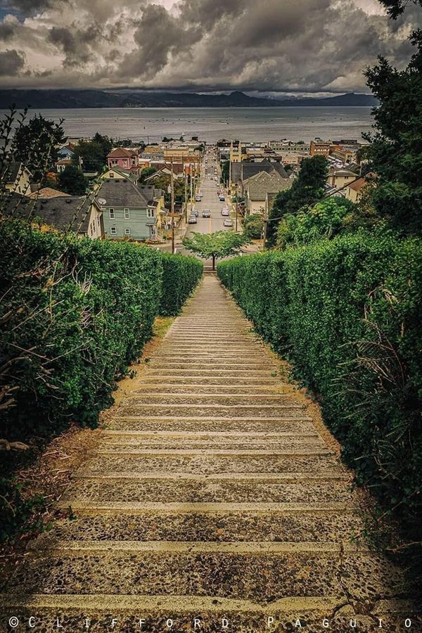 an old set of steps leading up to the ocean with houses on either side and clouds in the background