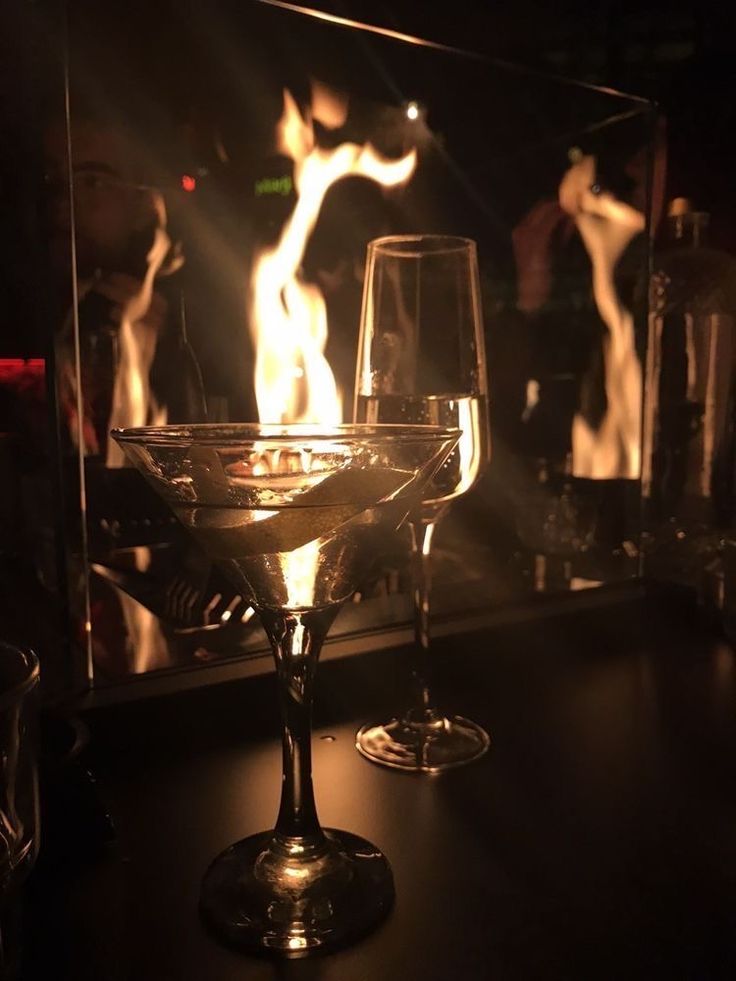 two wine glasses sitting on top of a table next to a fire in the fireplace