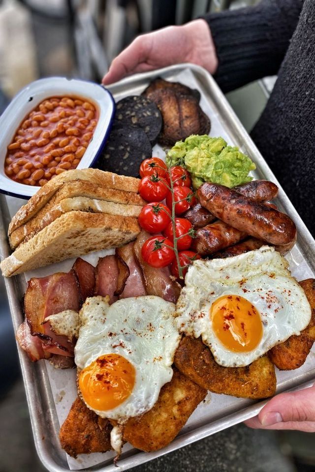 a person holding a tray with eggs, bacon, toast and other foods on it