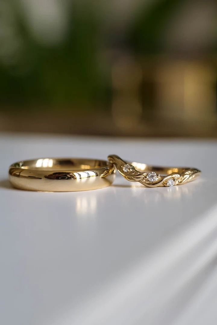 two gold wedding rings sitting on top of a white table next to each other,