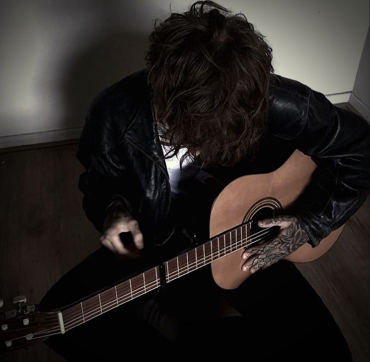 a man sitting on the floor playing an acoustic guitar