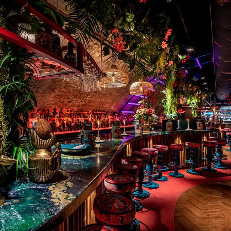 the interior of a restaurant with colorful lighting and potted plants on the bar counter