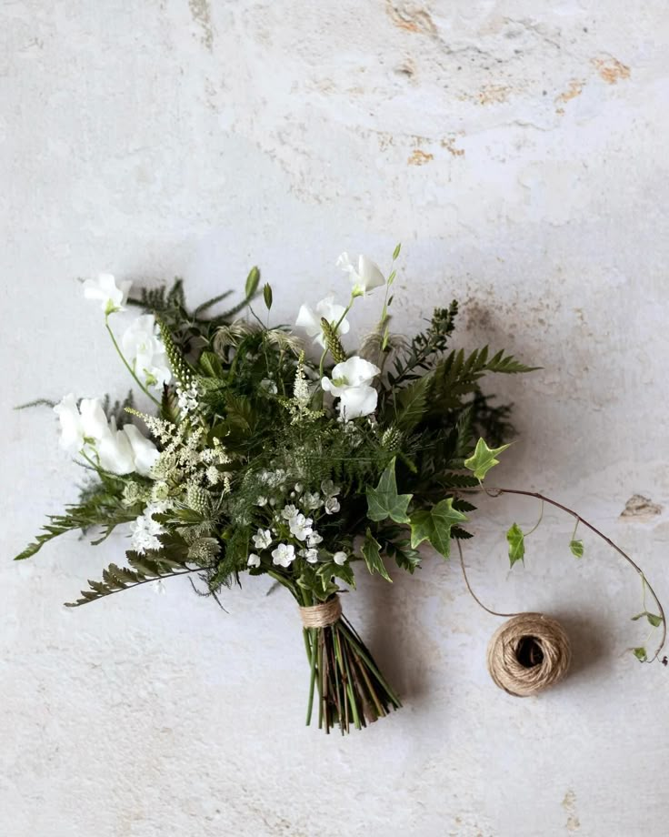 a bouquet of white flowers sitting next to a spool of twine