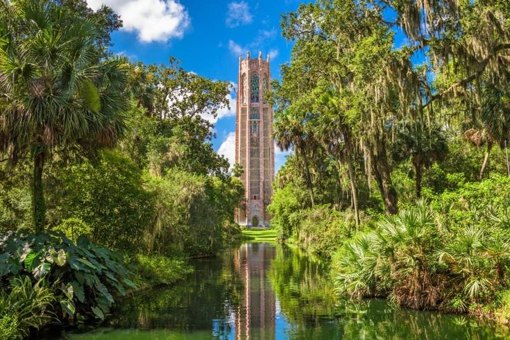 a tall tower towering over a river surrounded by lush green trees and palm trees on both sides