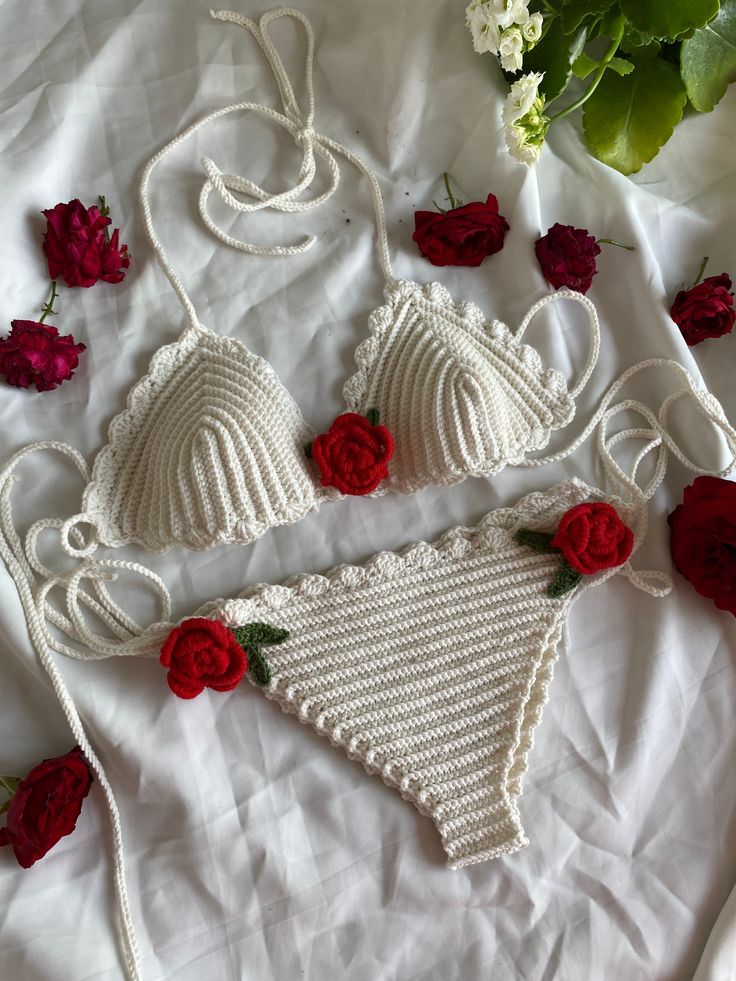 two white crocheted bikinis with red roses on the bed next to them