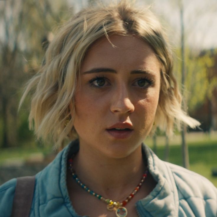 a close up of a person wearing a necklace and looking at the camera with a serious look on her face