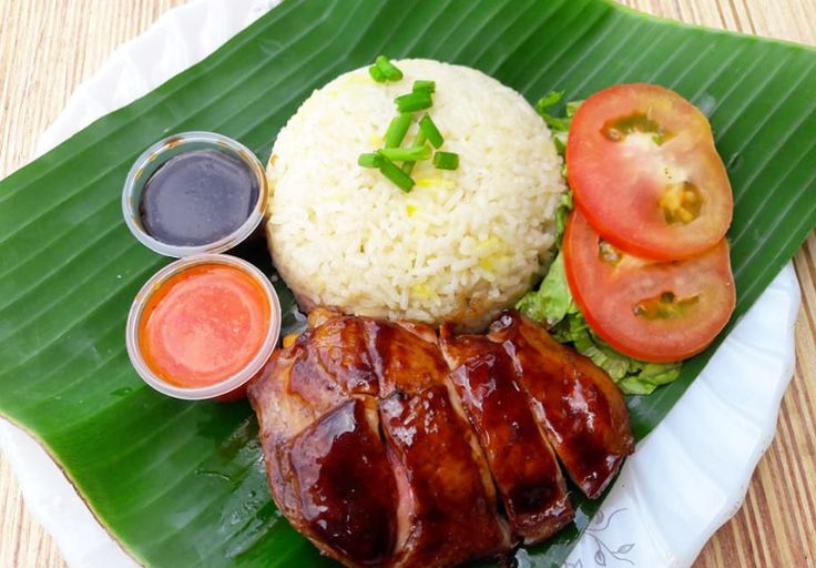 a plate topped with meat and rice next to sauces on a leafy green surface