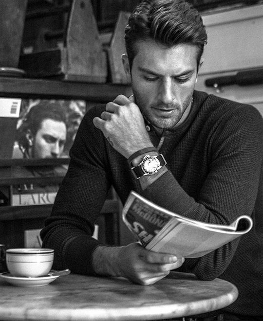 a man sitting at a table reading a newspaper and drinking coffee from a cup while holding his hand over his face