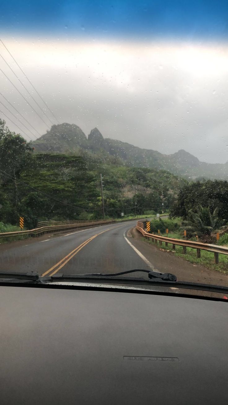 the view from inside a car driving down a mountain road with hills in the background